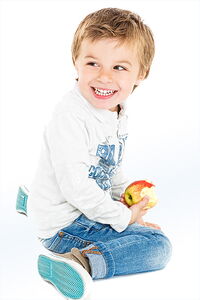 Kleiner Junge sitzt auf dem Boden - ©kreativloft.ch, stock.adobe.com nge mit Jeans und Pullover sitzt auf dem Boden hält einen angebissenen Apfel in der Hand. Er schaut nach hinten und lacht.